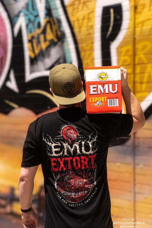Person wearing a black 'EMU Extort' t-shirt holding an EMU Export box in front of a colorful mural.